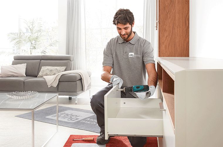 Monteur montiert Schublade in hellem Wohnzimmer.