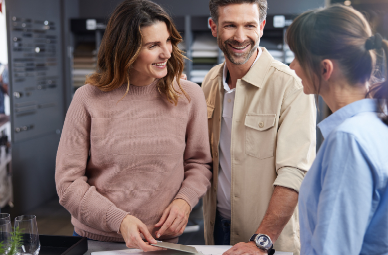 Beratungsgespräch in moderner Küchenausstellung mit einem Paar und einem Fachberater am Tisch.