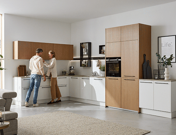 L-förmige Einbauküche in Weiß und Holzoptik mit zwei Personen.