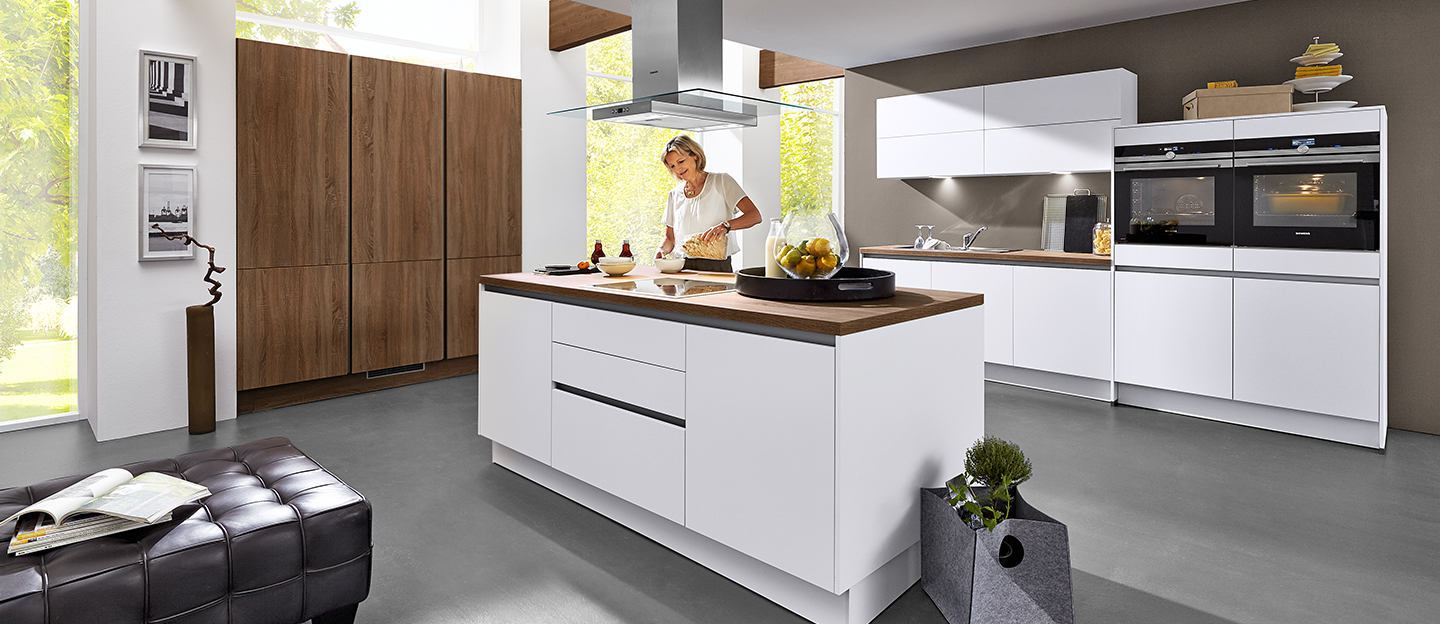 Frau in moderner weißen Küche mit Kochinsel und Holzdetails.