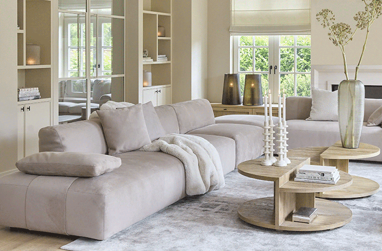 Ein hellbeiges Modulsofa, ergänzt durch runde Couchtische und Deko von RIVIÈRA MAISON.