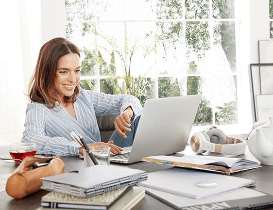 Frau arbeitet lächelnd am Laptop in einem hellen Büro.