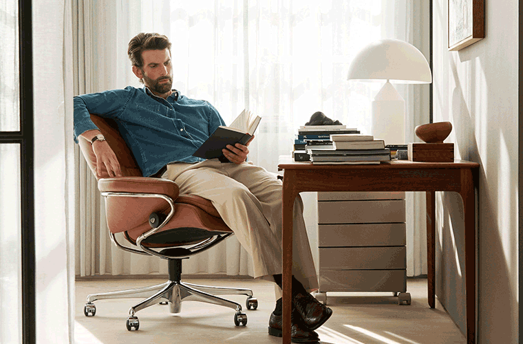 Mann liest entspannt in einem Stressless-Sessel an einem Schreibtisch.