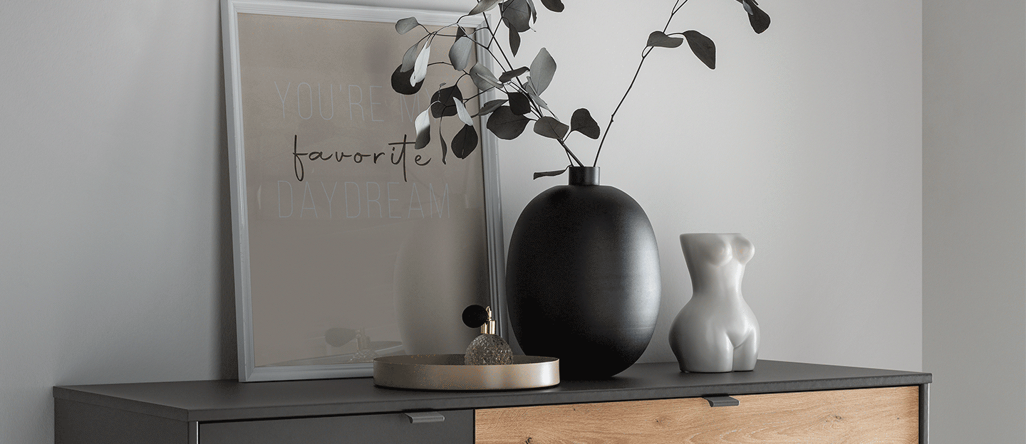 Kommode mit moderner Deko vor grauer Wand.