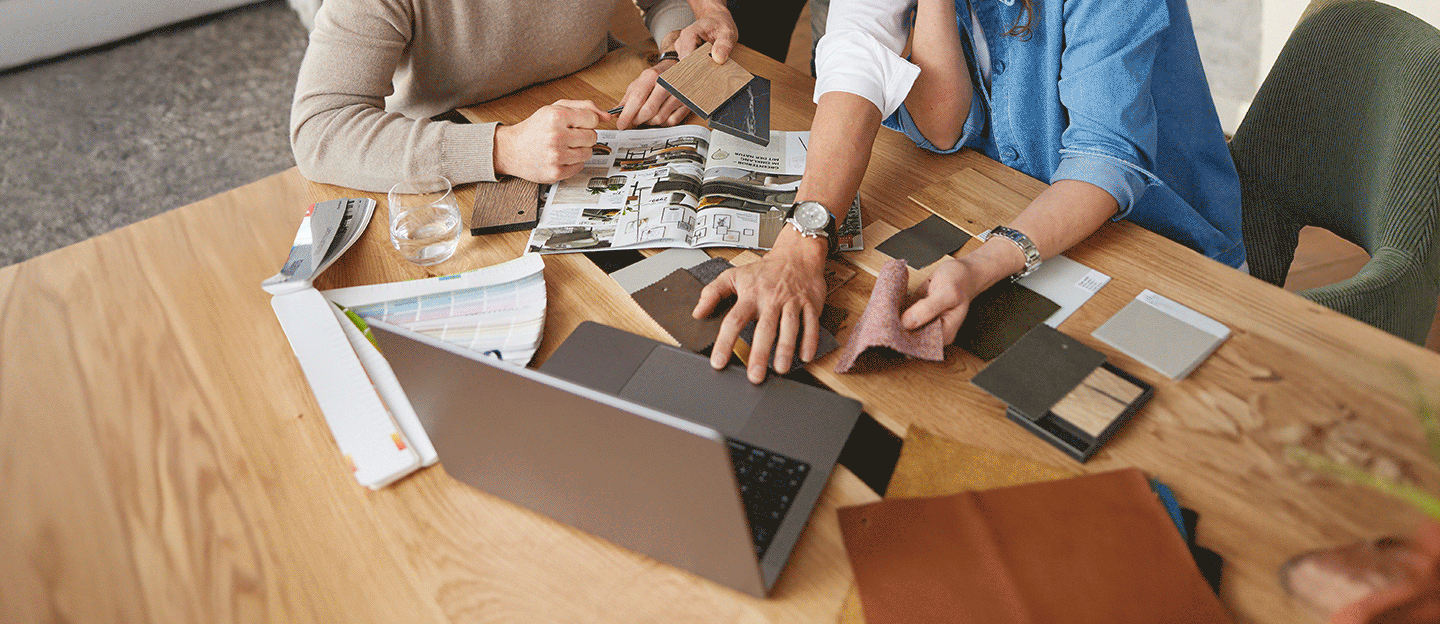 Zwei Personen sitzen an einem Laptop, welcher auf einem Holztisch steht.