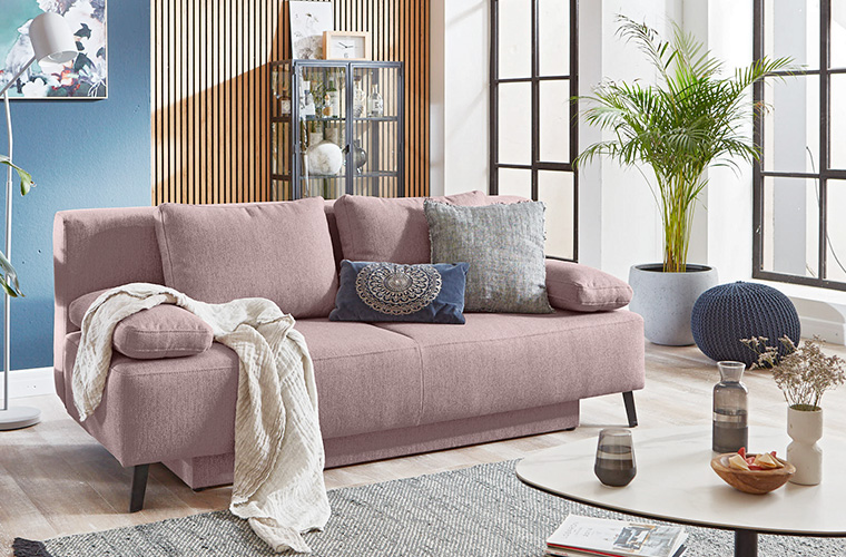 Frau bereitet in modernem Wohnzimmer ein Schlafsofa zum Ausziehen vor.