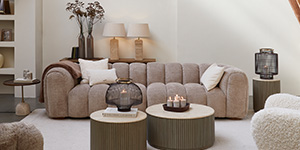 Ein hellbraunes Sofa steht hinter zwei Couchtischen aus Holz.