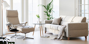 Heller Sessel und helles Sofa stehen bei einem kleinen Beistelltisch in einer modernen Wohnzimmerecke.