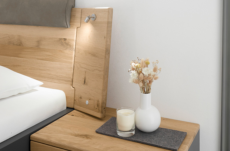 Hölzerner Nachttisch neben einem Bett mit Vase und Kerze.