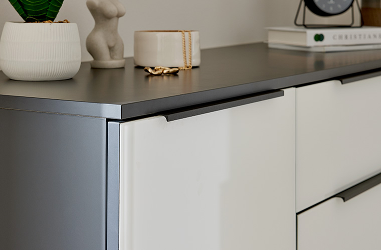 Nahaufnahme einer grauen Kommode mit weißen Details, auf welcher Deko liegt.