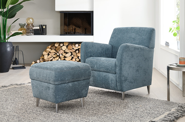 Hellblauer Polstersessel mit einem passenden Hocker, platziert in einem gemütlichen Wohnzimmer.