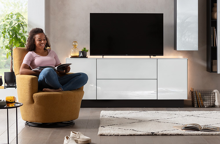 Eine Person sitzt entspannt auf einem senfgelben, runden Sessel.