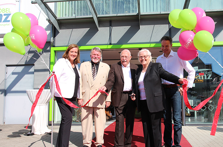 Eine Eröffnungsszene mit Ballons, bei der die Familie Janz ein Band durchschneiden.