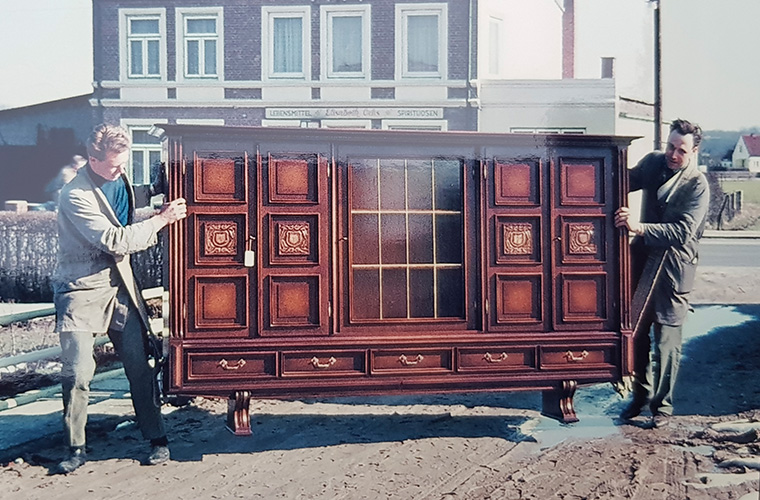 Zwei Personen tragen eine große, holzfarbene Kommode.