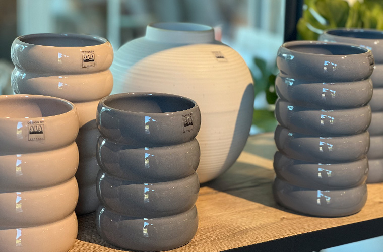 Viele runde Vasen in Grau und beige werden nebeneinander ausgestellt.