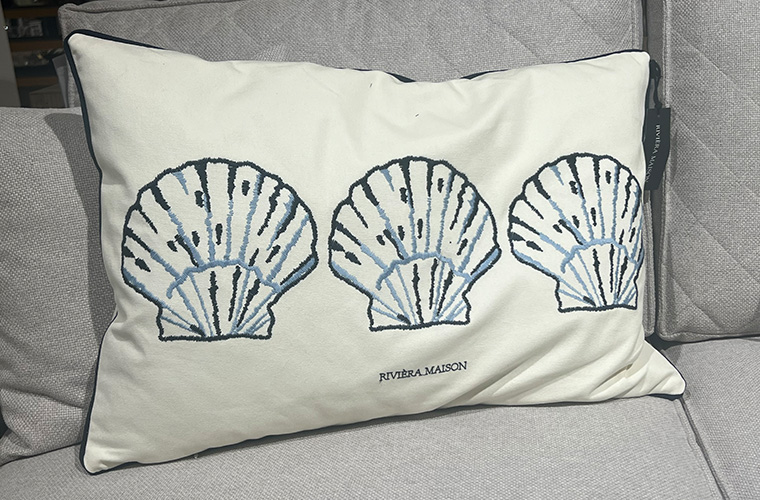 Kissen auf einer Couch mit einer Stickerei, die Muscheln in Blautönen zeigt.