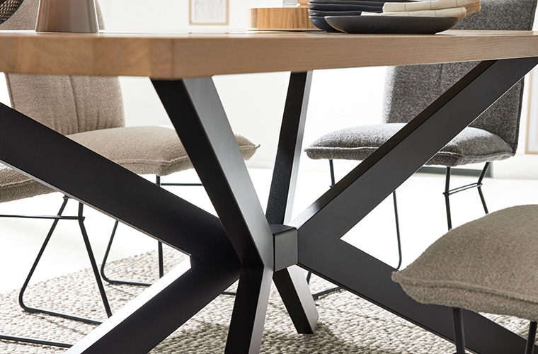 Detailansicht eines schwarzen Metallgestells, das eine hellbraune Holzplatte eines Esstisches trägt.