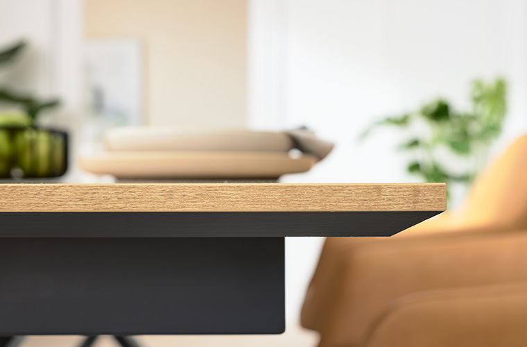 Detailaufnahme der Unterkonstruktion eines Tisches neben einem senfgelben, gepolsterten Stuhl.