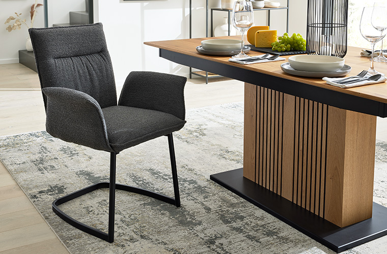 Schwarzer Stuhl mit Armlehnen, der an einem Esstisch mit Holzdetails steht.