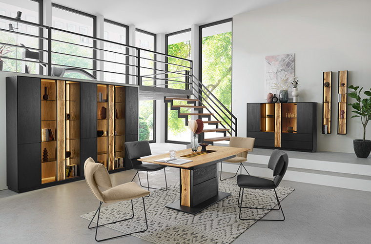 Essbereich mit Holztisch und Holzdetails, schwarzen Stühlen und dunklen Vitrinenschränken.