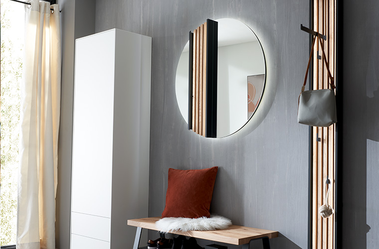 Helle Garderobenkombination mit einem runden, beleuchteten Spiegel.