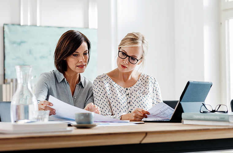 Zwei Frauen sitzen an einem Schreibtisch und besprechen etwas.