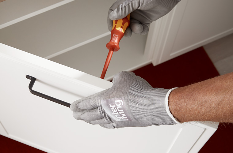 Nahaufnahme der Hand eines Monteurs mit Handschuhen, der eine Griffliste an einem Schrank festschraubt.