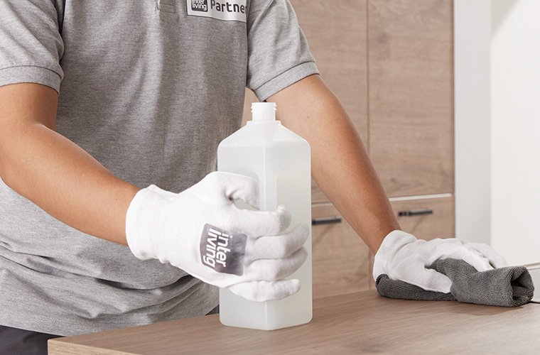 Nahaufnahme eines Monteurs mit Handschuhen, der eine Reinigungsflüssigkeit hält.