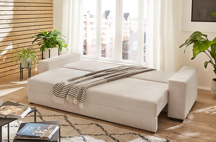 Helles Schlafsofa in beige, das zu einem Doppelbett ausgeklappt ist.