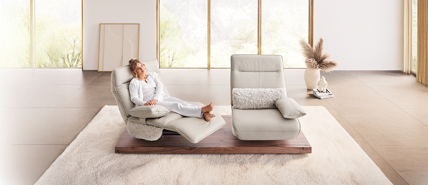 Frau sitzt entspannt in ihrem Wohnzimmer mit zwei hellen Sesseln.
