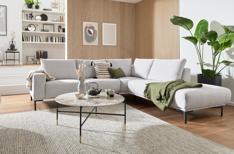 Modernes Wohnzimmer mit hellem Ecksofa, rundem Couchtisch, Teppich und dekorativen Pflanzen.
