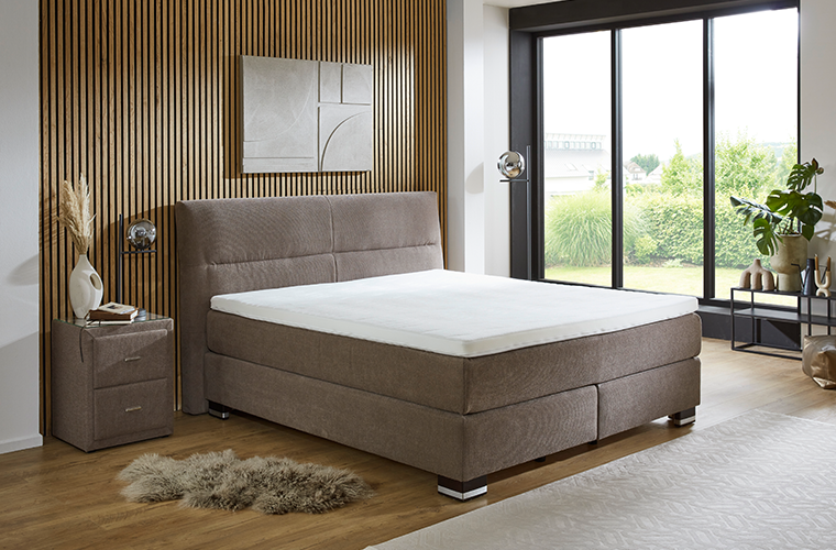 Polsterbett „Carlson“ in beige-braunem Stoff und mit hohem Kopfteil.