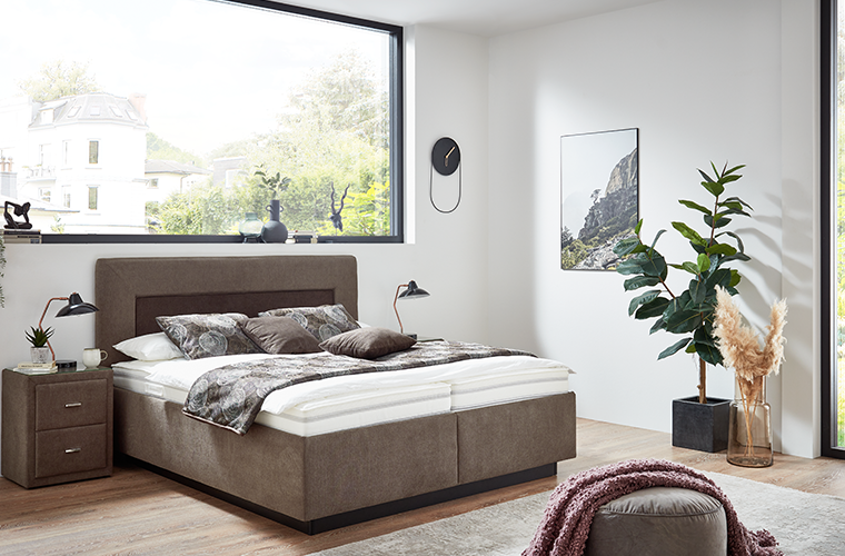 Bett „Naemi 2.0“ in braun mit gepolstertem Kopfteil.