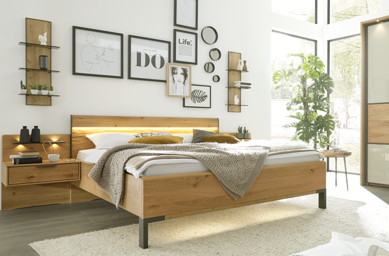 Bett „IL 1027“ in Holzoptik mit beleuchtetem Kopfteil in einem hellen Schlafzimmer.