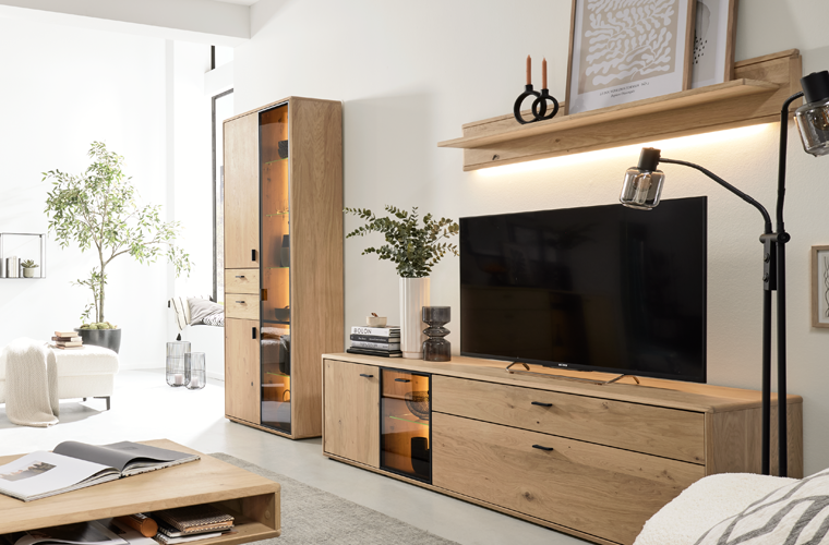 Wohnwand in Holzoptik mit TV-Board, Vitrine und Wandregal mit Beleuchtung in einem helen Wohnzimmer.