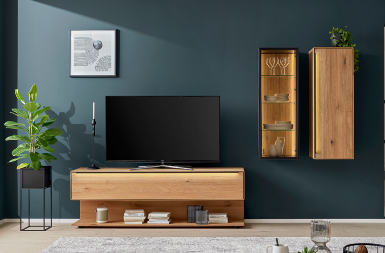 Wohnwand „IL 2033“ in Holzoptik mit TV-Board und hängenden Vitrinen in buntem Wohnzimmer.