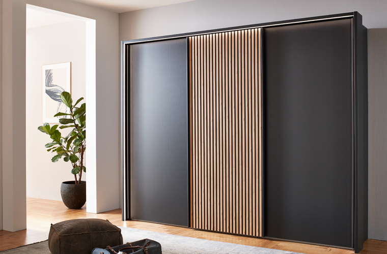 Kleiderschrank „Dom“ mit schwarzen Schiebetüren und Lamellen-Element in Holzoptik.
