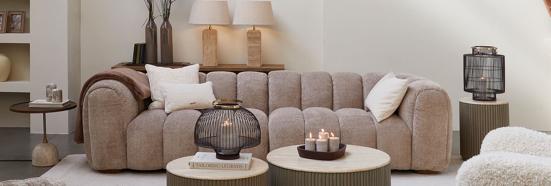 Beiges Sofa mit Kissen und runden Couchtischen mit Kerzen in einem gemütlichen Wohnzimmer.
