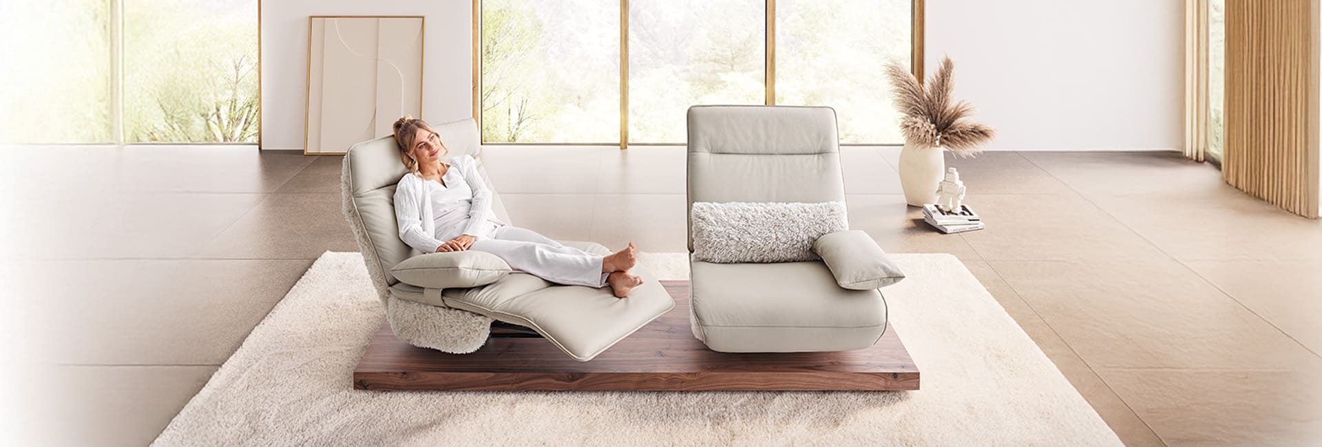 Frau sitzt entspannt in ihrem Wohnzimmer mit zwei hellen Sesseln.