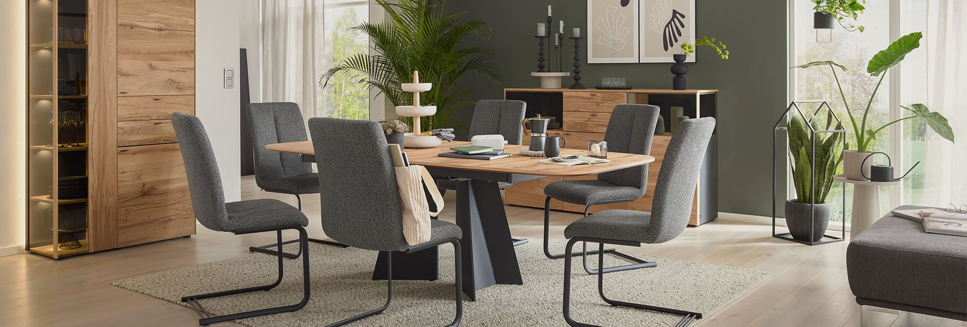 Esszimmer mit einem hellen Holztisch und grauen Stühlen, welches mit vielen grünen Pflanzen dekoriert ist.