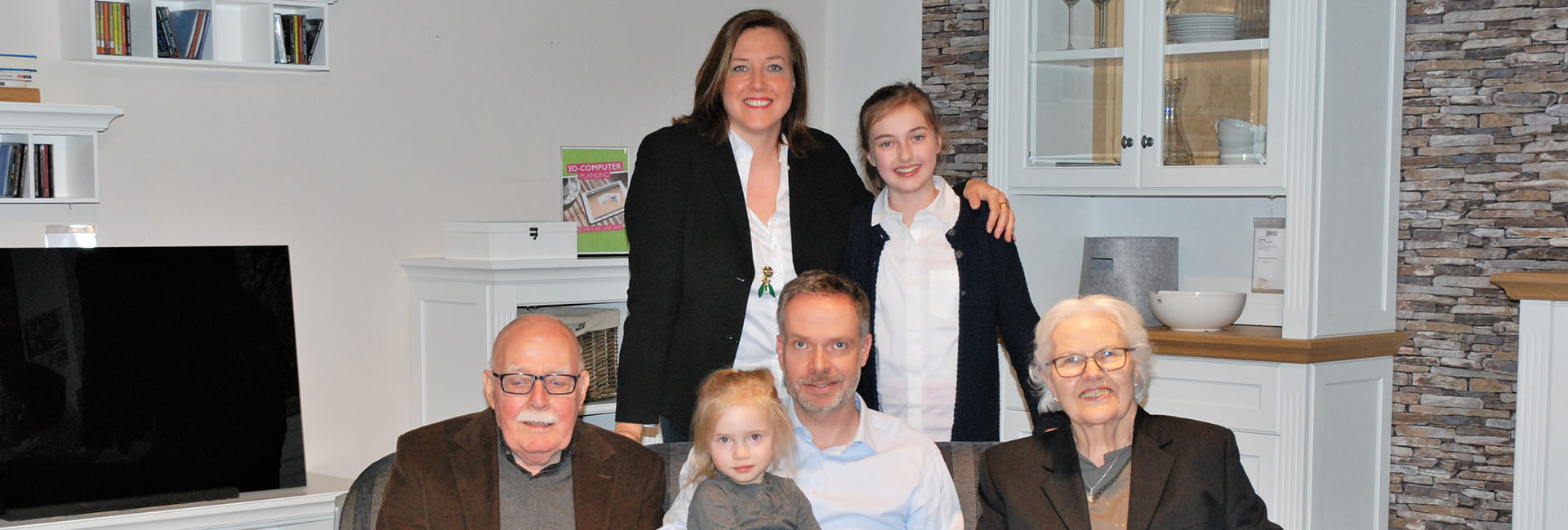 Mehrgenerationen-Familie Janz gemeinsam im Wohnzimmer sitzend und stehend.