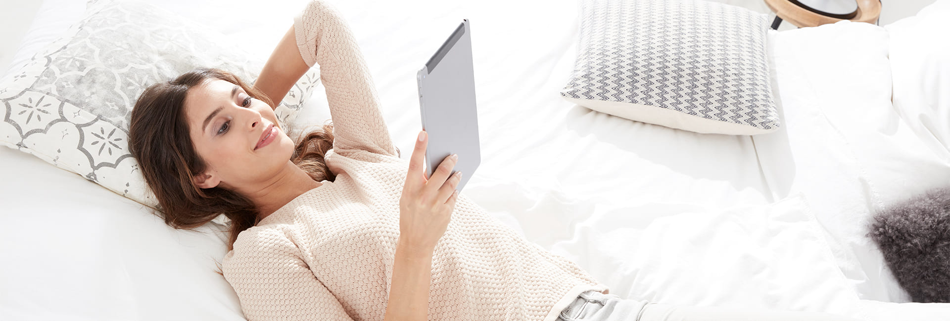 Frau liest in ihrem Bett etwas auf Ihrem Laptop.