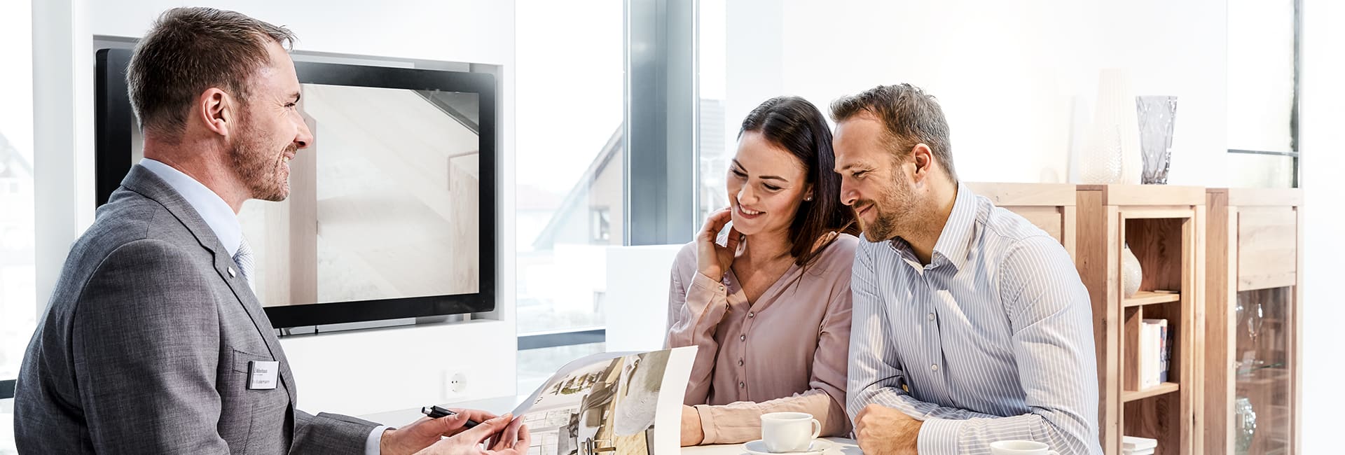 Berater spricht lächelnd mit einem jungen Paar in modernem Büro.